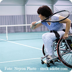 Eine Frau im Rollstuhl auf einem Tennisplatz holt zum Schlag mit dem Tennisschlger aus.